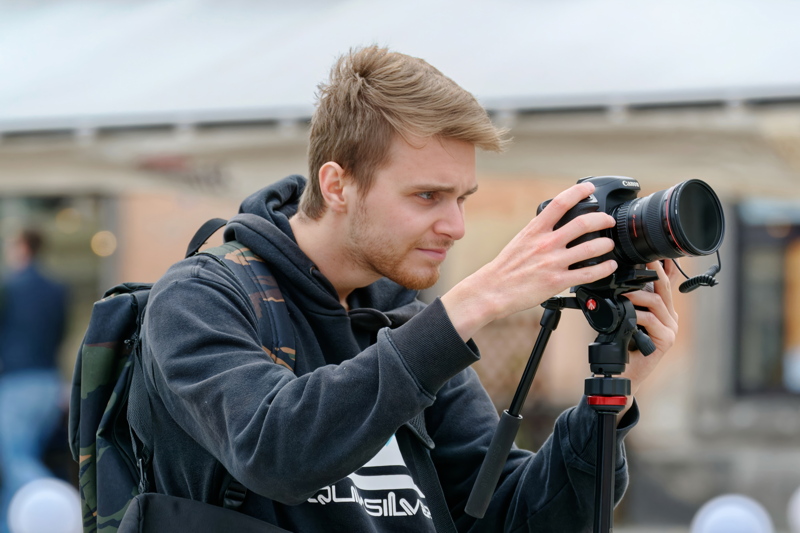 29 - Person focused on taking a picture with a black Canon camera mounted on a tripod